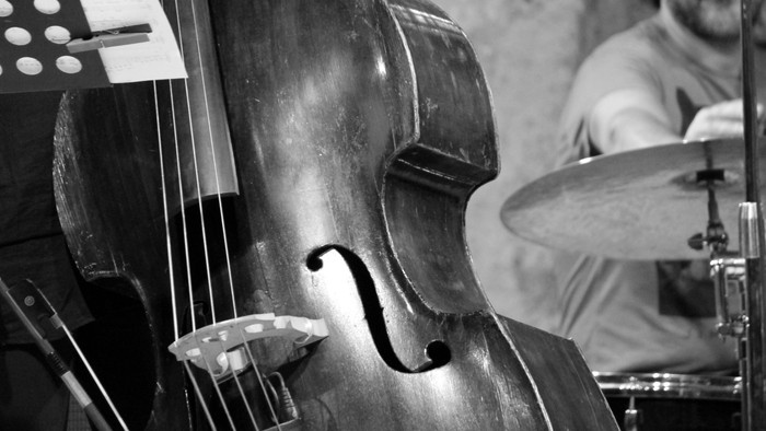 Detailaufnahme in schwarz-weiß von einem Kontrabass, im Hintergrund Schlagzeug
