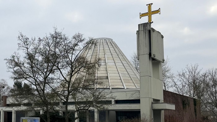 Moderne Kirchengebäude mit Kuppel und Kreuz, umgeben von schneebedeckter Landschaft und kahlen Bäumen.