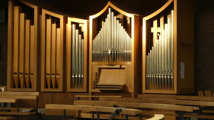 Elegante Kircheninnenausstattung mit einer großen Holzorgel und hölzernen Kirchenbänken unter Oberlichtern.