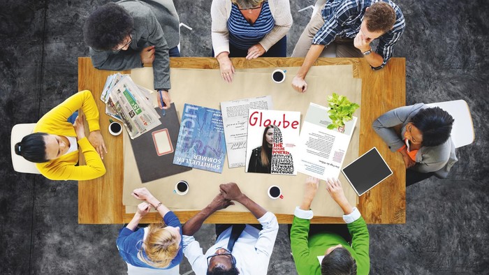 Eine Gruppe von Menschen sitzt um einen Tisch und arbeitet an einem Projekt.