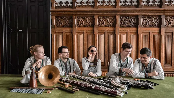 En gruppe spiller traditionelle instrumenter i et rigt udsmykket træværelse.