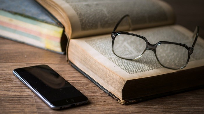 Brille, Handy und aufgeschlagenes Buch auf Holzplatte