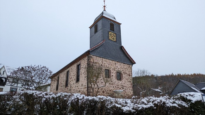Kleine Steinkirche mit Uhrturm, umgeben von Schnee.