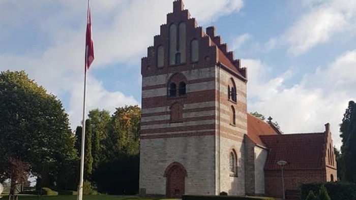 En kvinde går forbi en historisk bygning med tårn og flagstang.