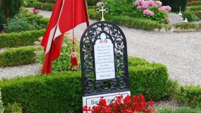 En grav med en dansk flag og røde blomster i en park.