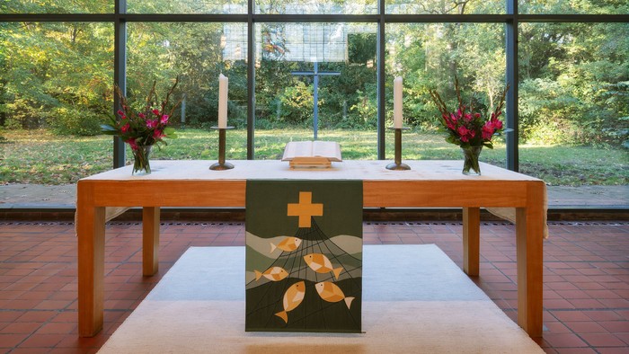 Moderner Kapellenaltar mit großen Fenstern, die die Natur zeigen, geschmückt mit Kerzen und Blumenarrangements.
