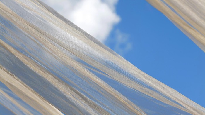 Durchscheinende Stoffbahnen, die einen strahlend blauen Himmel mit verstreuten Wolken einrahmen.