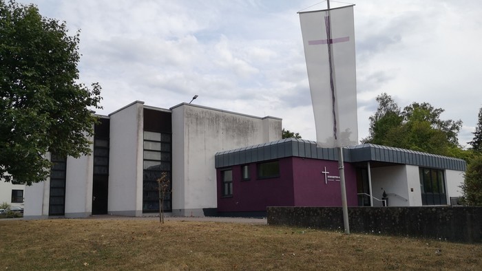Moderne Gebäude mit Kreuzsymbol auf der Flaggenstange, umgeben von Bäumen und Gras.