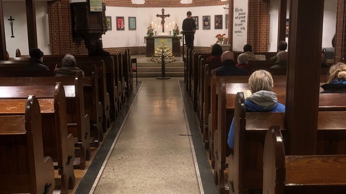 Kirchengang mit Holzbänken und Kreuz in der Mitte
