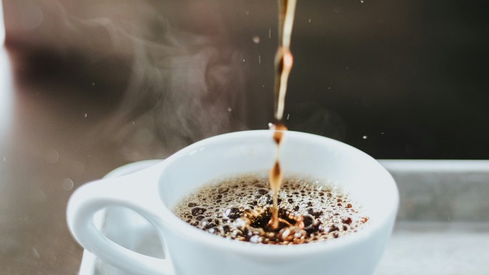 Kaffee wird in eine weiße Tasse auf einem Tablett gegossen
