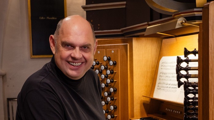 Mand sitter ved et orgel og smiler til kameraet