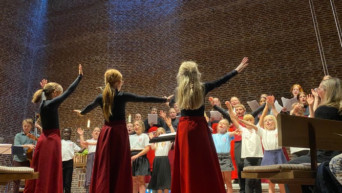 En gruppe kvinder i røde skørter og sorte topper danser på en scene foran en publikum.