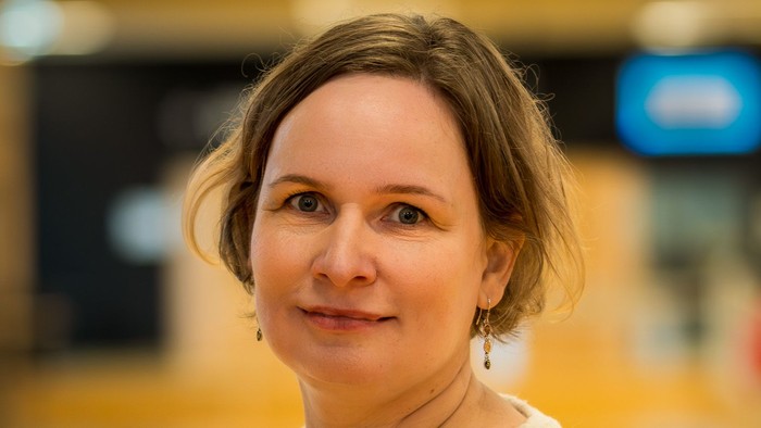 En smilende kvinde i en lys blondebluse poser indendørs med en sløret baggrund.