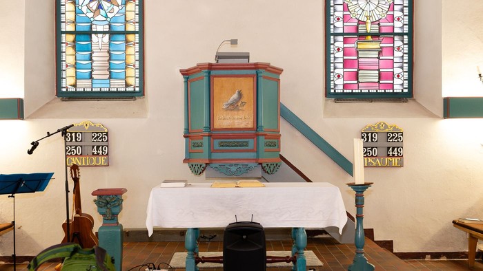 Bunte Kanzel- und Altaraufstellung in einer Kirche mit bunten Glasfenstern und nummerierten Sitzplatzschildern.
