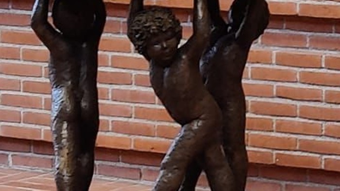 Bronzefigur af to børn, der bærer en plate på et murstenvægge