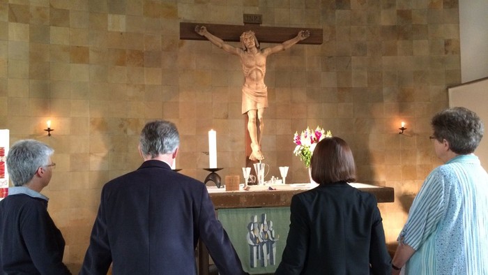 Vier Personen beten vor einem Kruzifix in einer Kirche