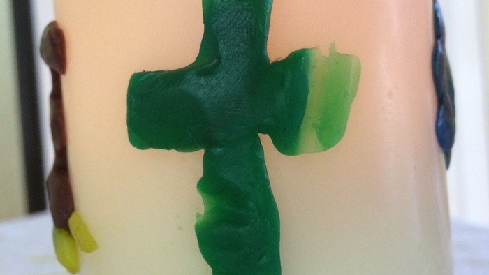 Ein grüner Kreuzaufkleber auf einer weißen Kerze