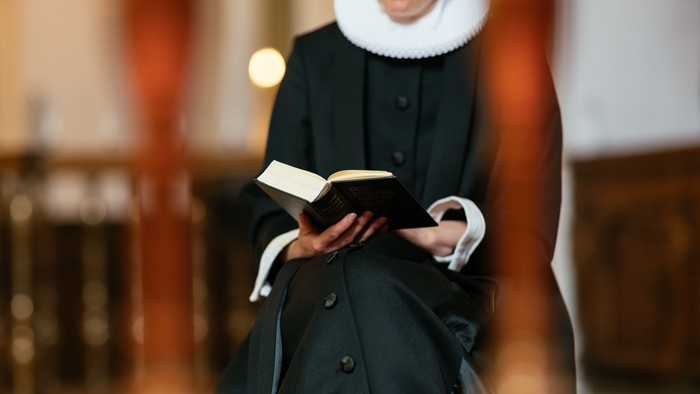 En person i traditionelt religiøst tøj læser i en åben bog i en kirkelig omgivelse.