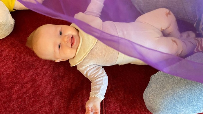 Baby ligger på rød underlag og holder en violet bånd.