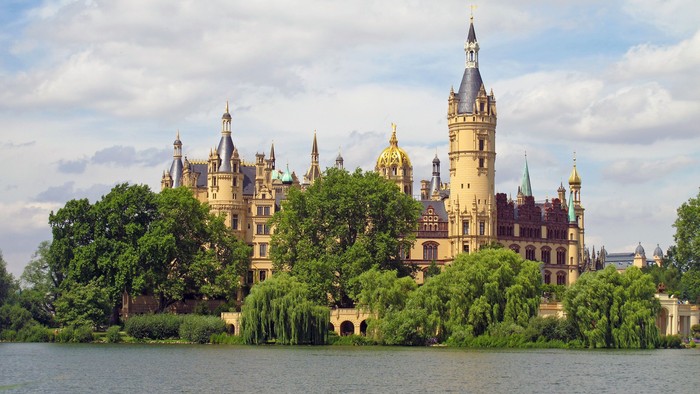 Mächtiges Schloss auf einer üppig grünen Insel, umgeben von einem ruhigen See unter einem teilweise bewölkten Himmel.