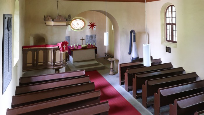 Idyllisches Kapelleninneres mit hölzernen Kirchenbänken, Altar und schlichten religiösen Verzierungen.