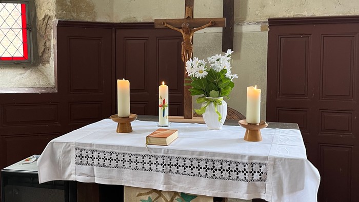 Ein Tisch mit Kerzen, Blumen und Kreuz in einem Raum