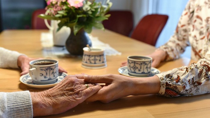 Zwei Menschen halten sich sanft an den Händen, während sie gemeinsam an einem gemütlichen Tisch Tee genießen.