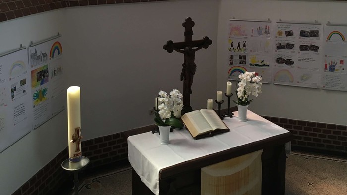 Weißer Altar mit Kreuz und Kerzen vor buntem Kirchenfenster