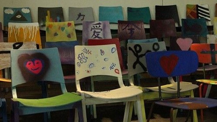 Kreative Stühle mit bunten bemalten Motiven und herzlichen Kunstwerken, ausgestellt in einem Klassenzimmer.