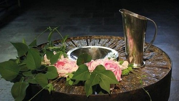 Elegante Holzschale hält eine silberne Karaffe neben einem Strauß rosa Rosen und Grünzeug.