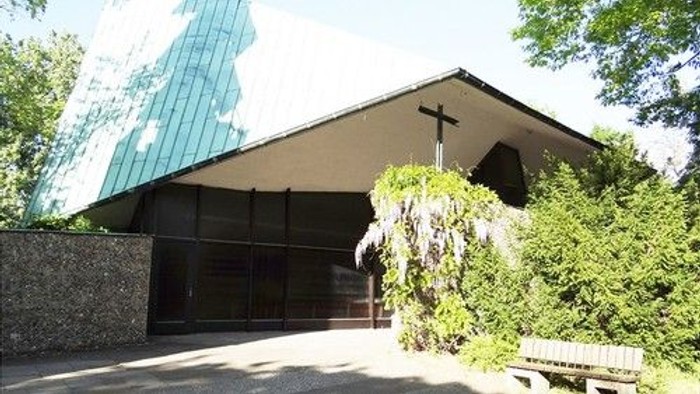 Moderne Kirche in Berlin Neu-Westend mit schrägem Dach, Kreuz und üppigem Grün, das einen ruhigen Eingangsbereich umgibt.
