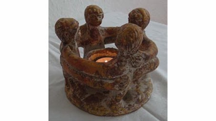 Handgefertigter Stein-Kerzenhalter in Form von vier sitzenden Figuren, die eine brennende Kerze im Inneren halten.
