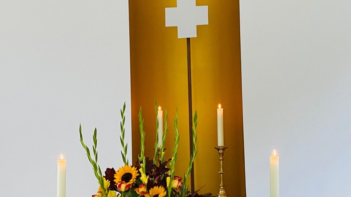 Eleganter Altar mit lebhaften Blumen, Kerzen und einem goldenen Kreuz hinter einem erleuchteten Fenster.