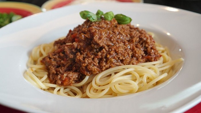 En ret med spaghetti og biff i tomatsoace på en hvid tælle.