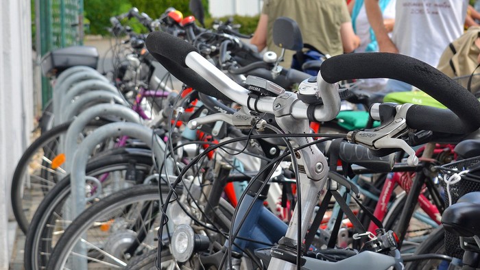 Nahaufnahme mehrerer abgestellter Fahrräder in einer Reihe; im Vordergrund Lenker und Bremsen eines Fahrrads scharf im Fokus, dahinter verschwimmen weitere Räder und einige Menschen im Hintergrund.
