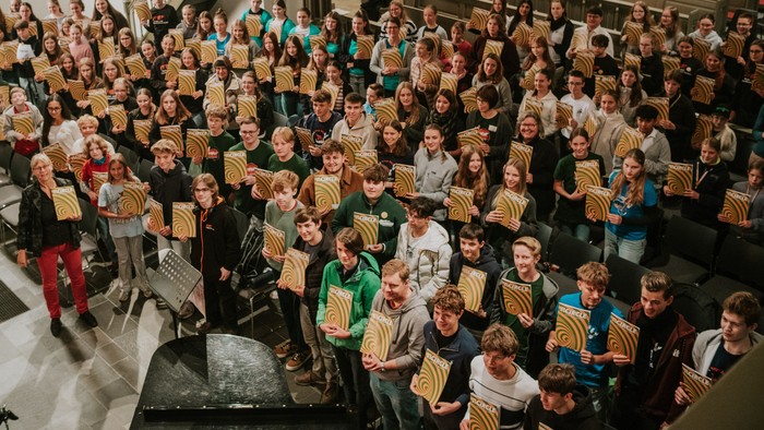 Große Gruppe von Menschen, die identische gelb-schwarze Plakate in einem prächtigen Innenraum halten.