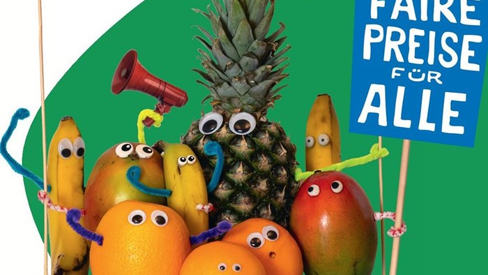 Bunt inszeniertes Bild mit Obstfiguren (Banane, Ananas, Mango, Orangen) mit aufgeklebten Augen und Armen, die wie Demonstrierende wirken; eine Figur hält ein Megafon, daneben ein Schild mit der Aufschrift „Faire Preise für alle“.