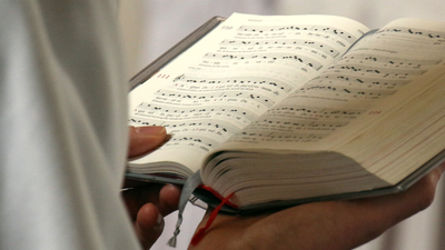 Person hält aufgeschlagenes Buch mit Noten
