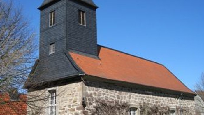 Außenansicht der evangelischen Kirche in Bründersen von Südwesten. Natursteingebäude mit rotem Ziegeldach und dunklem Turm.