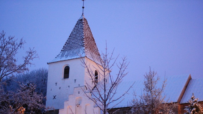 En lille kirke med tårn og blå tag i snefaldende landskab