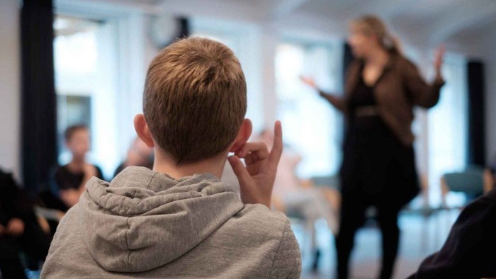 En ung dreng i graugul hodie giver rosken mens en kvinde i baggrunden danser.