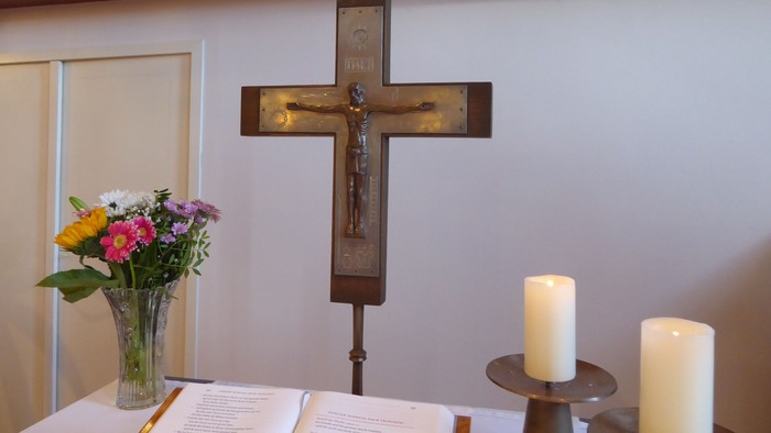 Religiöser Altar mit Kruzifix, Blumen, einem aufgeschlagenen Buch und brennenden Kerzen.