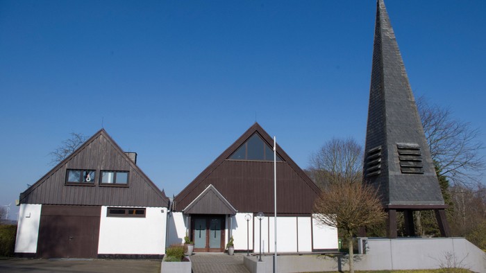 Moderner Bau mit dreieckigen Dächern und hohem Turmspitz unter klarem, blauem Himmel.