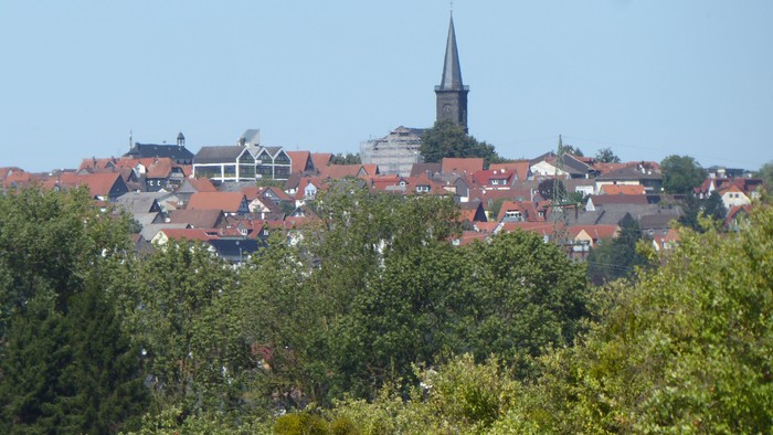 Idyllisches Städtchen mit roten Hausdächern und einem markanten Kirchturm, der sich über üppiges Grün erhebt.