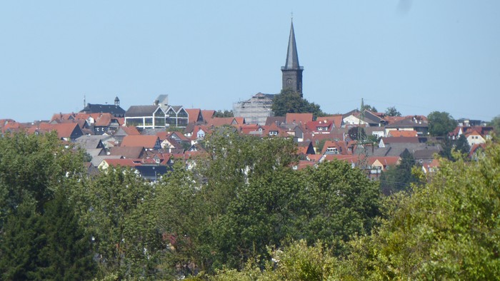Idyllisches Städtchen mit roten Hausdächern und einem markanten Kirchturm, der sich über üppiges Grün erhebt.