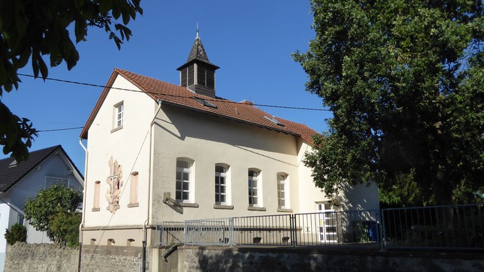 Idyllische weiße Kirche mit kleinem Turm und rotem Dach, eingebettet in eine grüne, ruhige Nachbarschaft.