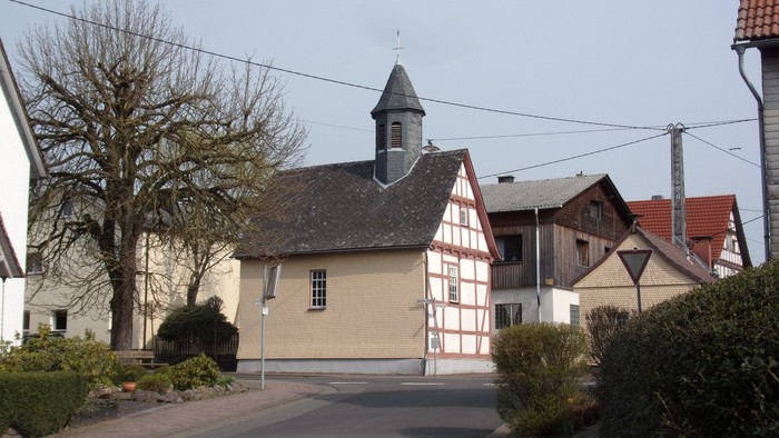 Idyllische Dorfkapelle mit Fachwerkbau und kleinem Glockenturm in einer ruhigen Nachbarschaft.