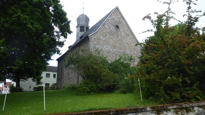 Steinkirche mit Glockenturm, umgeben von Wiese.