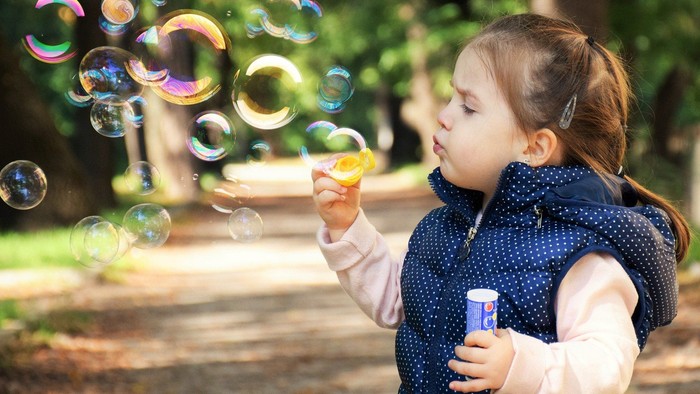 Et lille barn blæser boblebubbler i en park