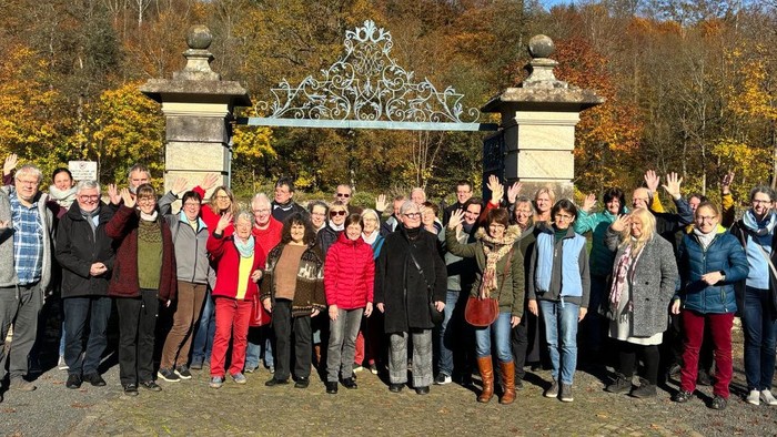 Eine fröhliche Gruppe posiert gemeinsam vor einem verzierten Tor im Herbst und zeigt Friedenszeichen.